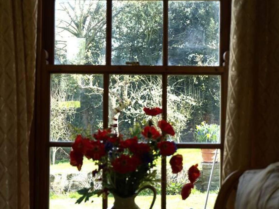 A living room with a window showing a garden and flowers in a vase at Cottage Sleeps 2 Garden Parking Ryton