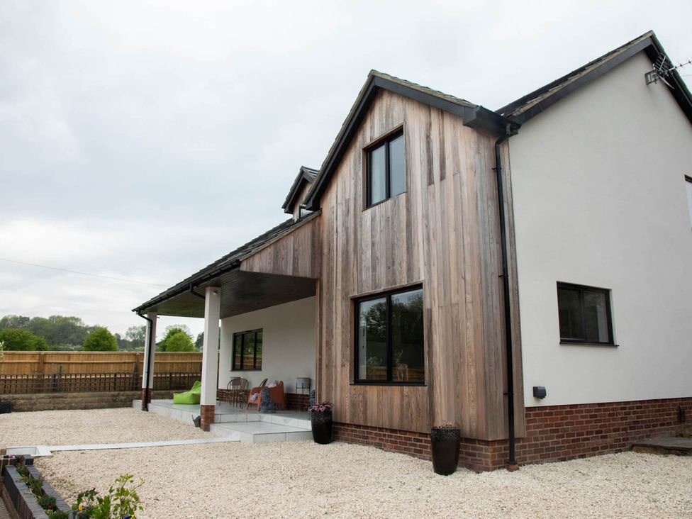 An exterior view of a house with wooden features and a gravel area at House Sleeps 10 with Enclosed Garden Checkendon near Henley-On-Thames