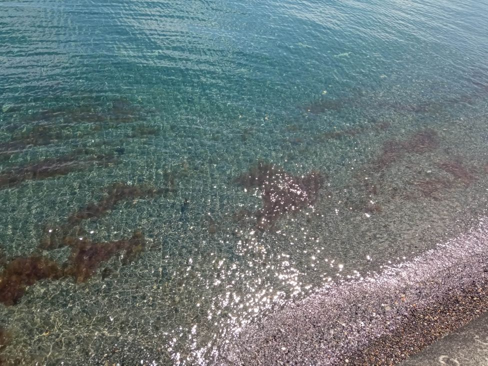 A clear view of the water with sand and rocks at the shore