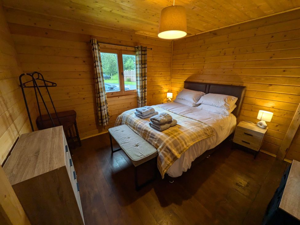 A bedroom with a bed and nightstand at Pet Friendly - Lodge at Riverview Holiday Park, Mangerton near Newcastleton