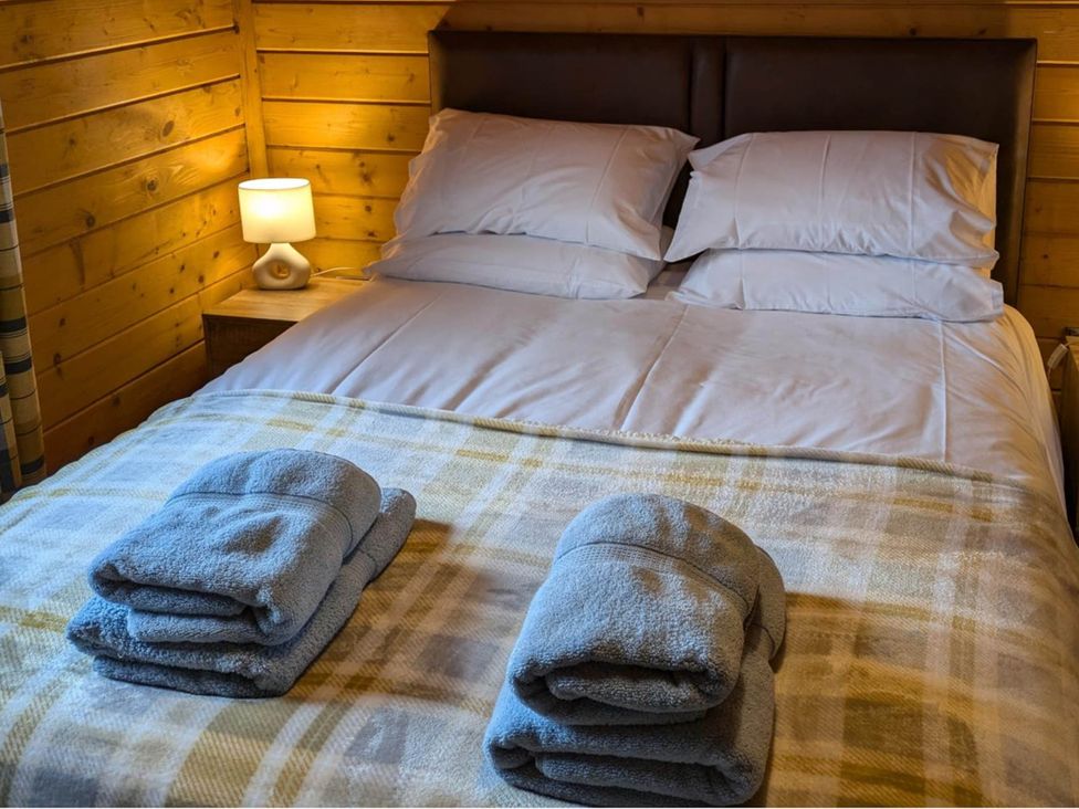 A bedroom with a bed, lamp, and towels at Pet Friendly - Lodge at Riverview Holiday Park, Mangerton near Newcastleton