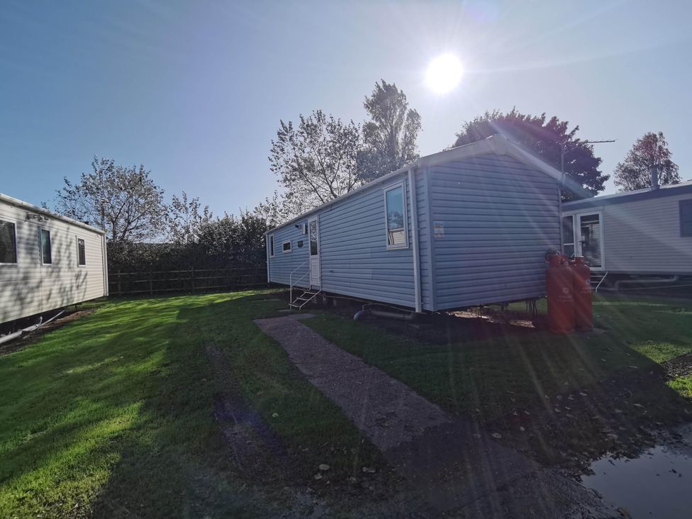 A static caravan with gas bottles and trees at 8Berth- SmartTV- CloseToBeach- FamilyFriendly in Mablethorpe