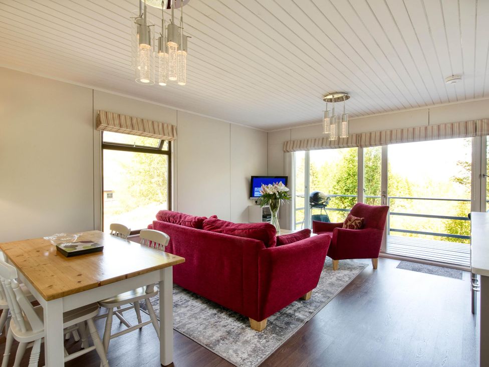 A living room with a sofa, armchair, dining table and television at 2 bedroom lodge with stunning loch, mountain views Crianlarich