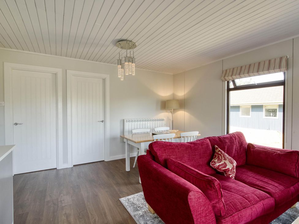 A living room with a red sofa, dining table and chairs at 2 bedroom lodge with stunning loch, mountain views in Crianlarich