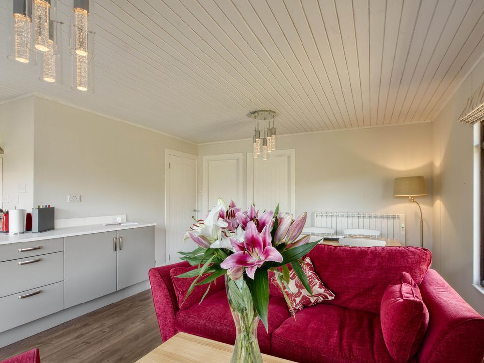 A living room with a red sofa and flowers on a table at 2 bedroom lodge with stunning loch, mountain views in Crianlarich
