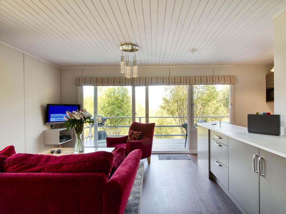 A living room with a sofa, TV, and kitchen counter at 2 bedroom lodge with stunning loch, mountain views Crianlarich