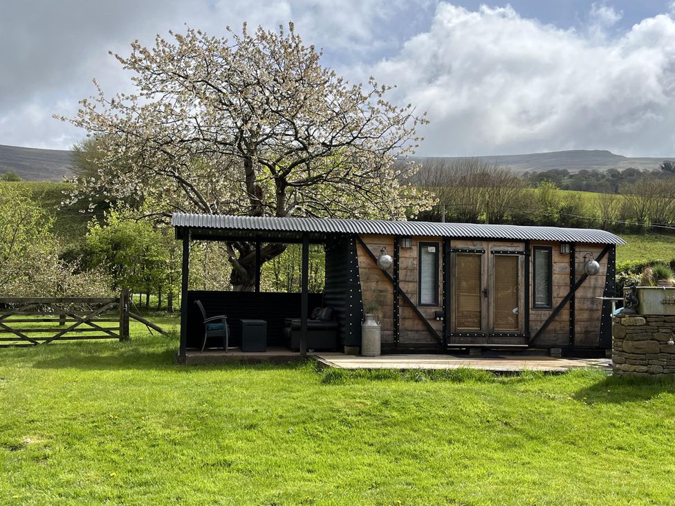A cabin with a porch and surrounding trees at Transformed Railway Wagon- Sleeps2-Garden-Firepit in Powys near Crickhowell