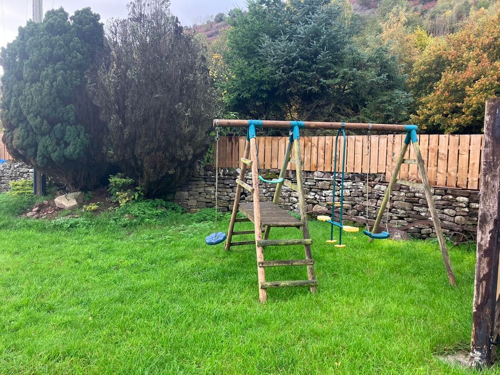 A garden with a swing set and trees at Transformed Railway Wagon- Sleeps2-Garden-Firepit near Crickhowell