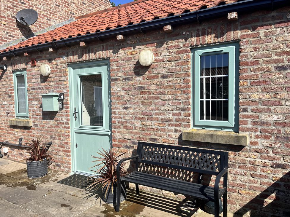An outdoor entrance with a bench and plants at TBC