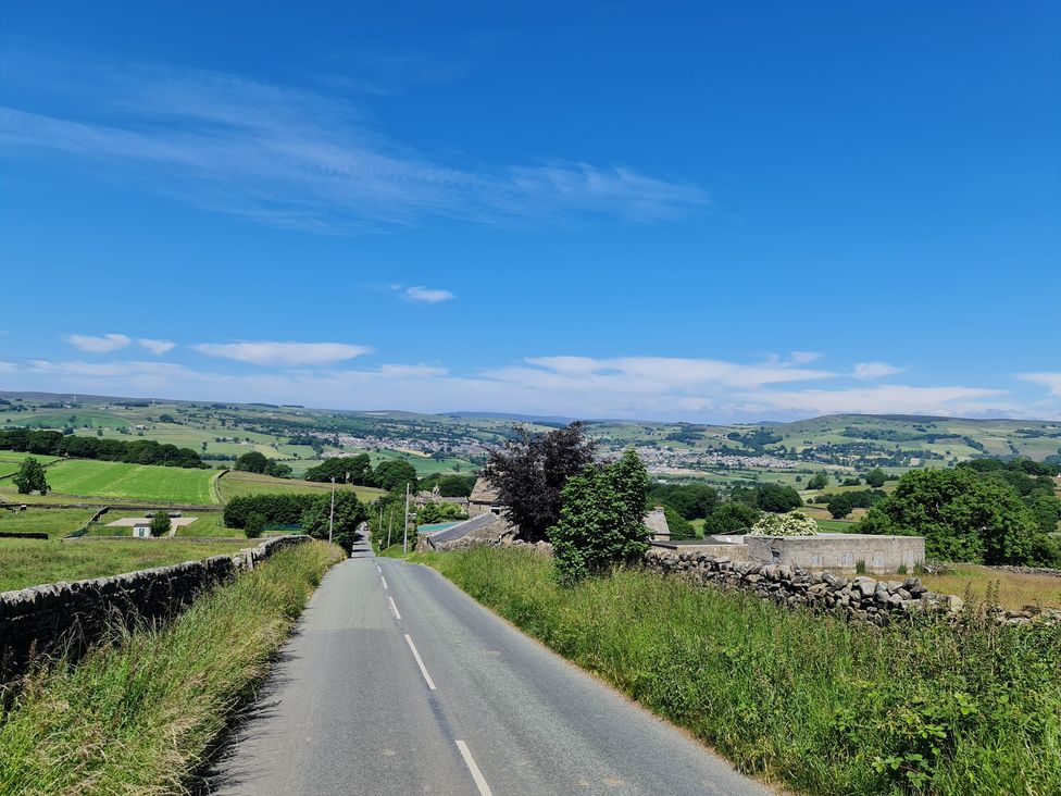 A road leading through fields with trees and buildings at TBC