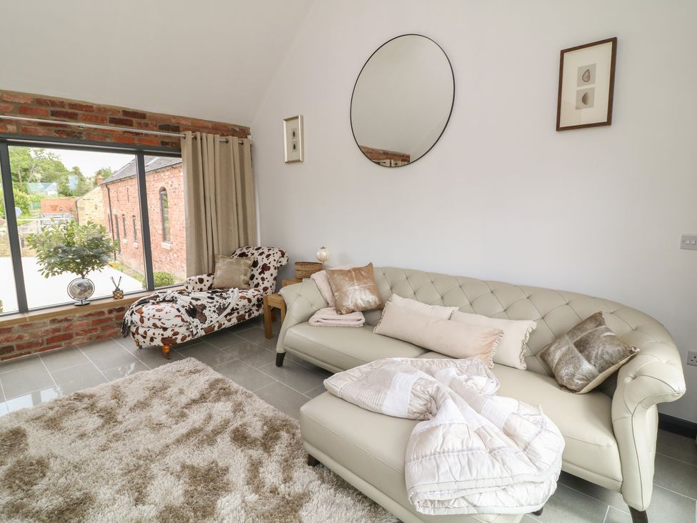 A living room with a sofa, armchair, and large window at The Croft, Home Farm in Ripley
