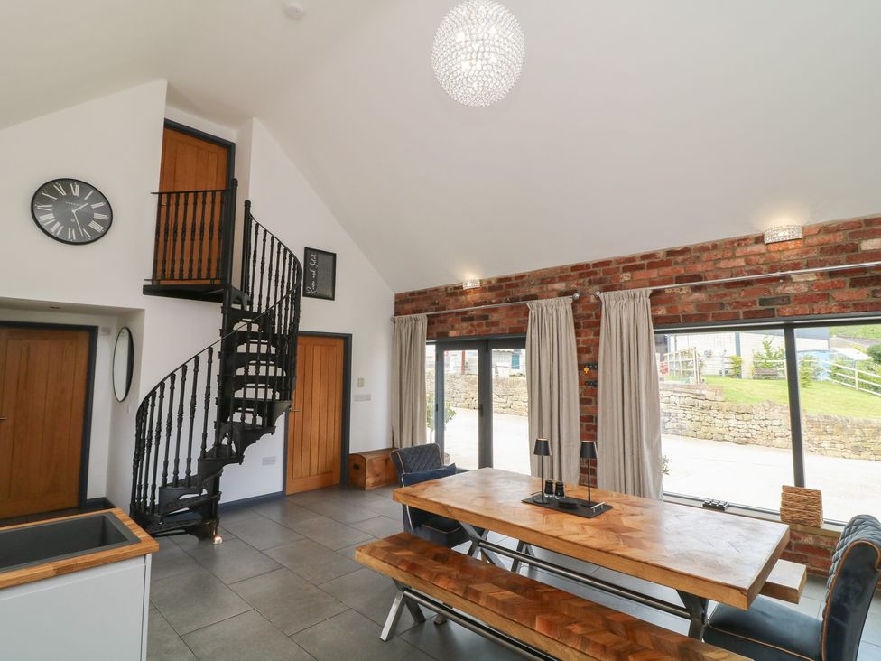 A dining room with a spiral staircase and wooden table at The Croft, Home Farm in Ripley
