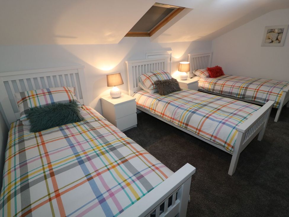 A bedroom with three beds and a lamp on a nightstand at The Cartwheel in Amroth