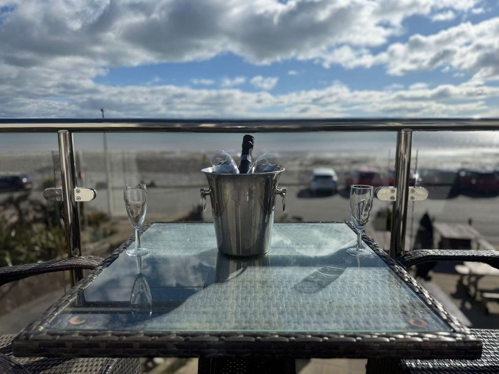 A balcony with a champagne bucket and glasses overlooking the beach at The Cartwheel in Amroth