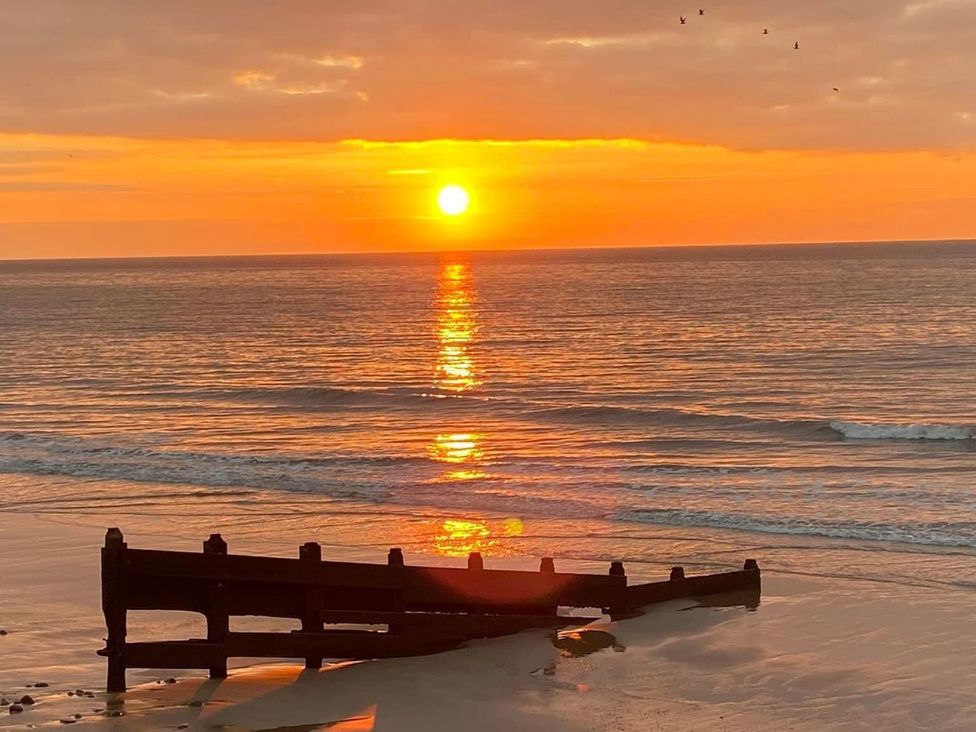 A sunset over the ocean with a pier on the beach at The Cartwheel in Amroth
