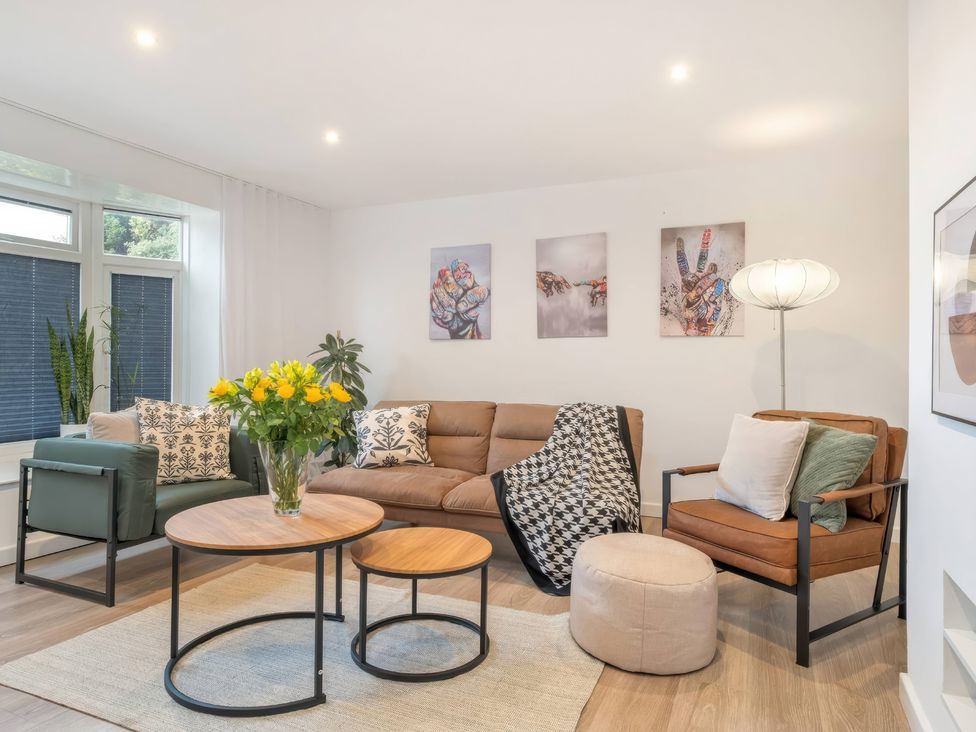 A living room with a sofa, two chairs, coffee table and plants at TBC 