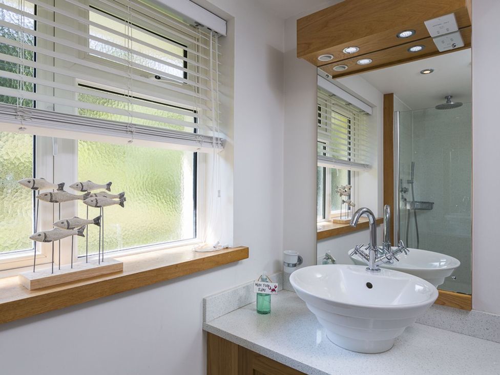 A bathroom with a sink, mirror, and shower at 6 Knowle Court in Salcombe