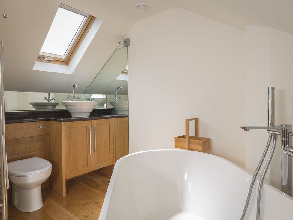 A bathroom with a bathtub, toilet, and sinks at 6 Knowle Court in Salcombe