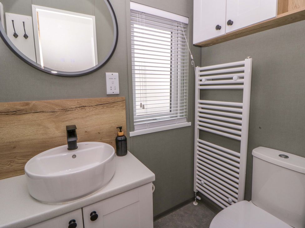 A bathroom with a sink, mirror, toilet, and radiator at The Dorchester at Bay View in New Quay