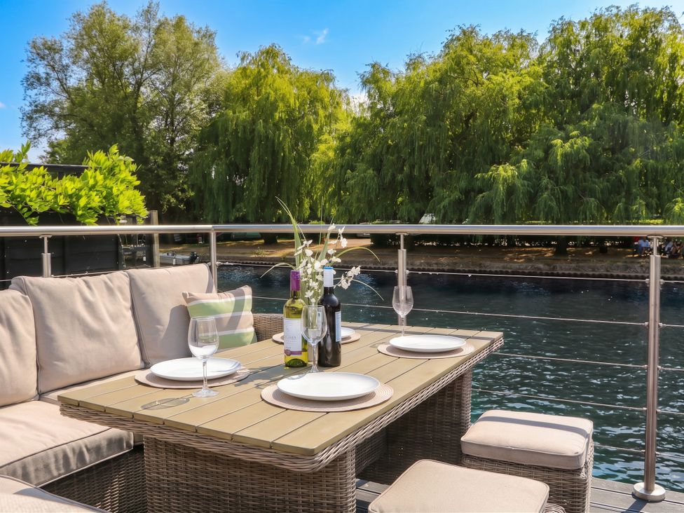 An outdoor dining area with a table and chairs by the water at Island Cottage Rod eyot Henley-on-Thames