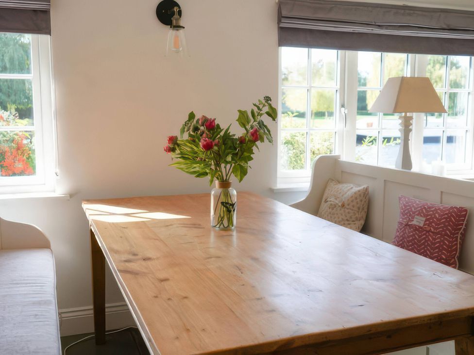 A dining room with a wooden table and flowers in a vase at Island Cottage Rod eyot Henley-On-Thames