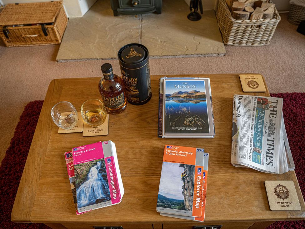 A living room with a coffee table featuring drinks, books, and a newspaper at Edengrove, Aberfeldy