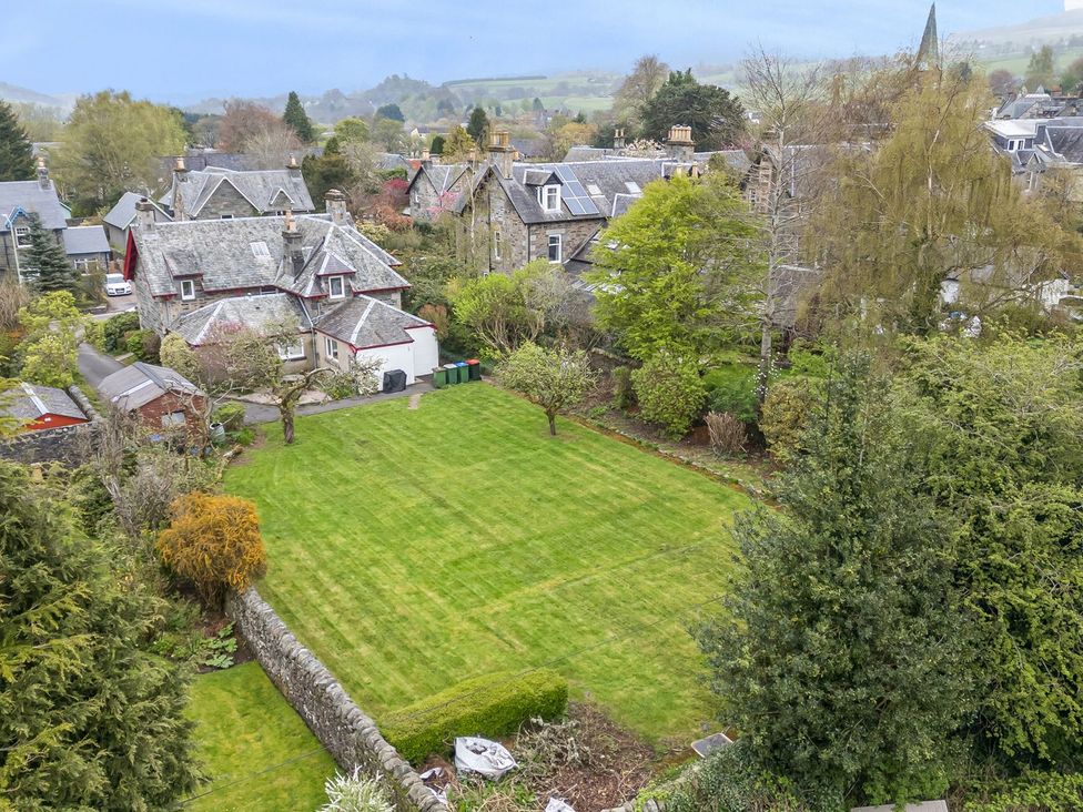 A garden with grass and houses in the background at Edengrove Aberfeldy