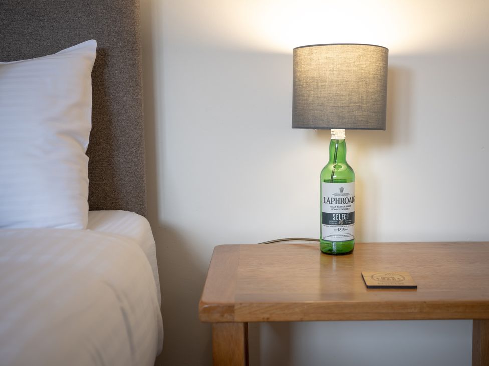 A bedside table with a lamp and a bottle at Edengrove in Aberfeldy