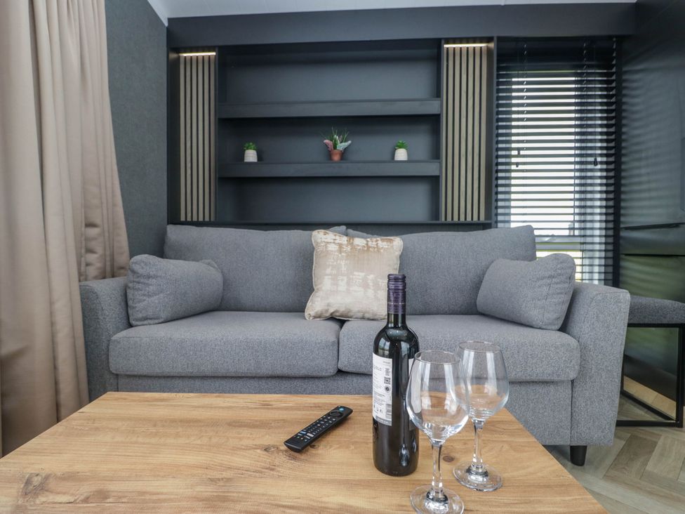 A living room with a sofa, table, wine bottle, and glasses at Heron in Haverigg