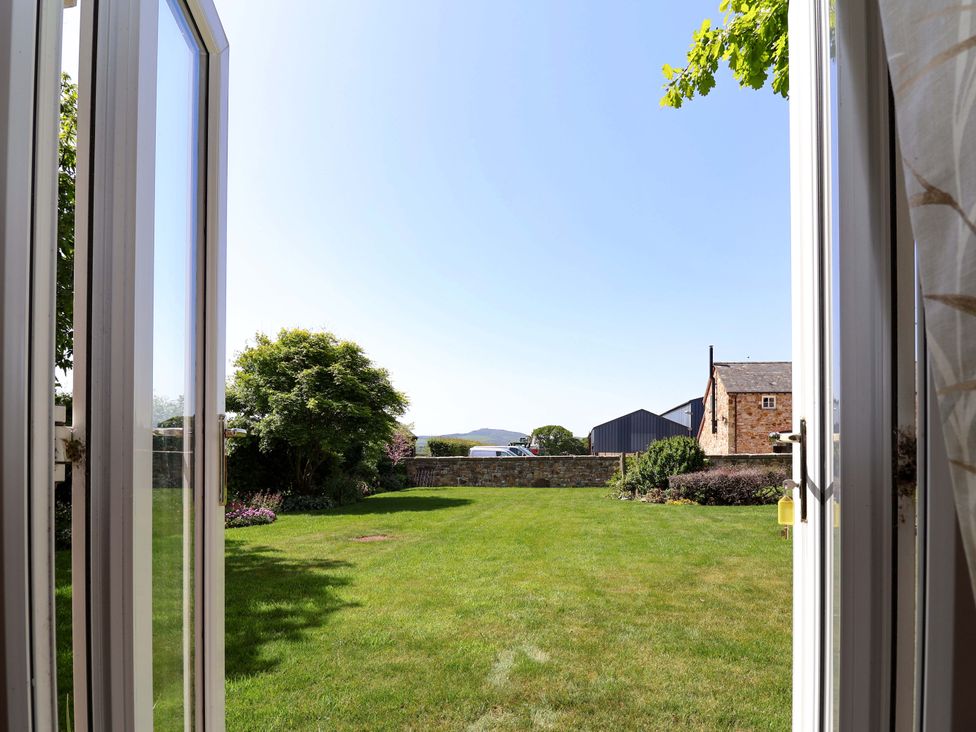 A view of a garden with grass and trees from an open window at Ty Haf in Rhosemor