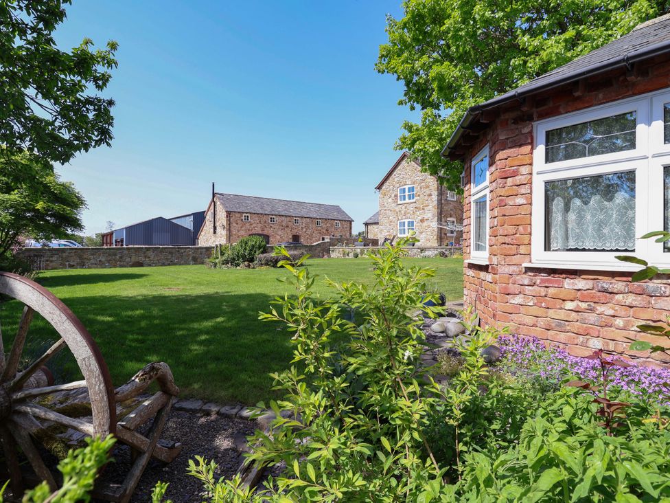 A garden with grass and brick buildings at Ty Haf in Rhosemor