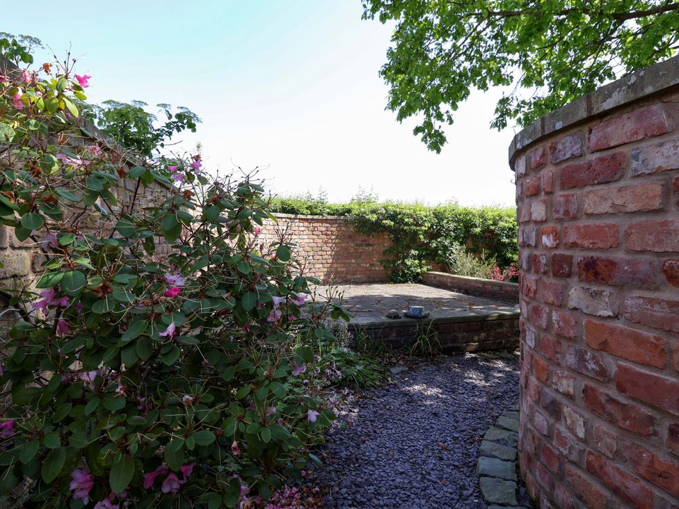 A garden with flowers, brick wall and a tiled area at Ty Haf in Rhosemor