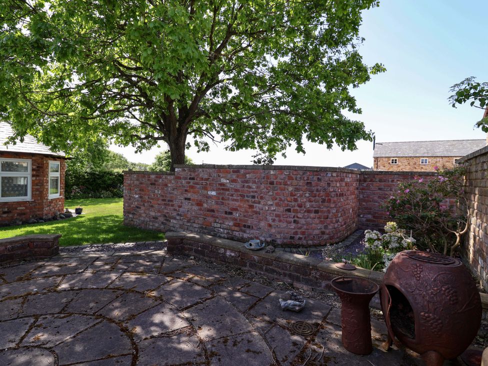 A garden with a brick wall and tree at Ty Haf Rhosemor