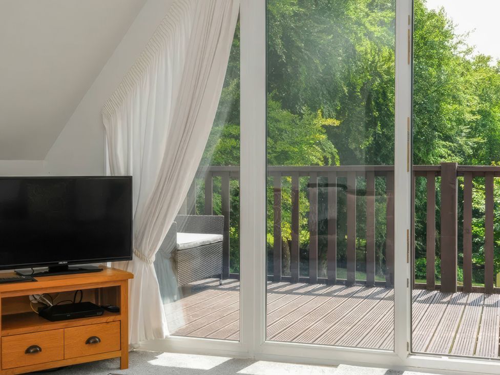 A living room with a television and sliding door to the deck at 9 Honicombe Park in Callington