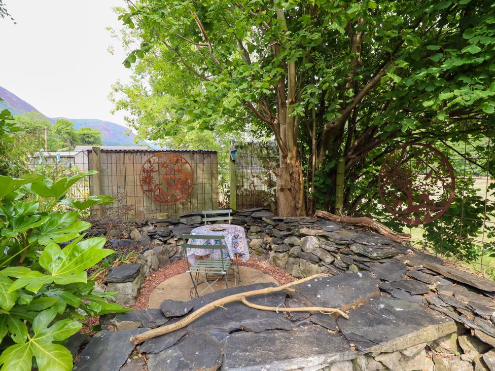 A garden with a stone seating area and table at Hud Y Coed in Llangynog