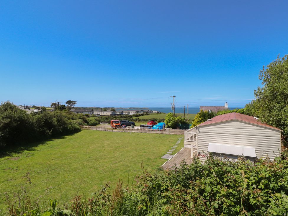 A view of a grassy area with a caravan and vehicles at Mor a Mynydd in Pwllheli