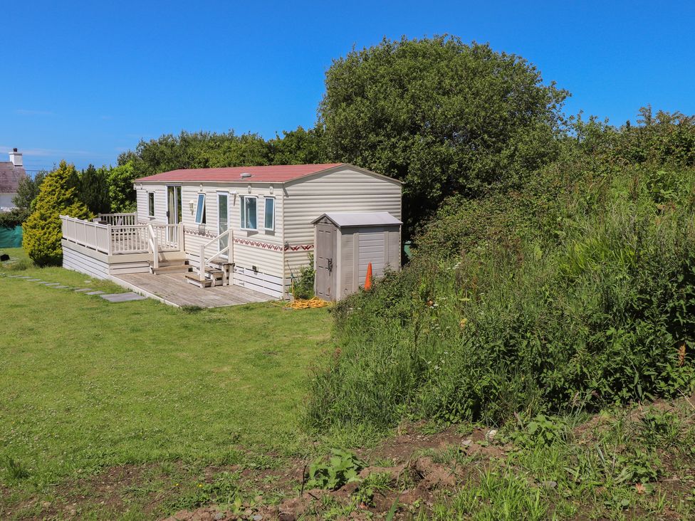 A mobile home with a deck and a shed in an outdoor area at Mor a Mynydd in Pwllheli