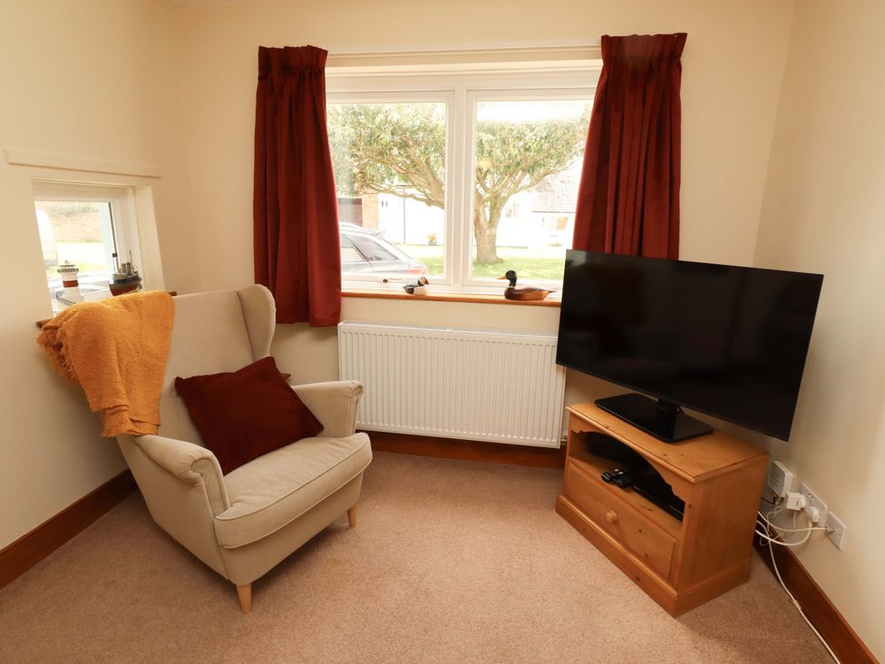 A living room with an armchair and a television at Sarah's Cottage