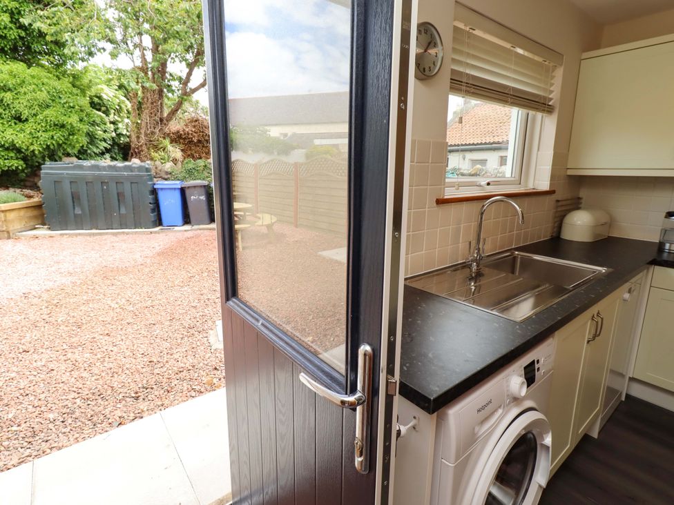 A kitchen with a sink and washing machine leading to a backyard at Sarah's Cottage