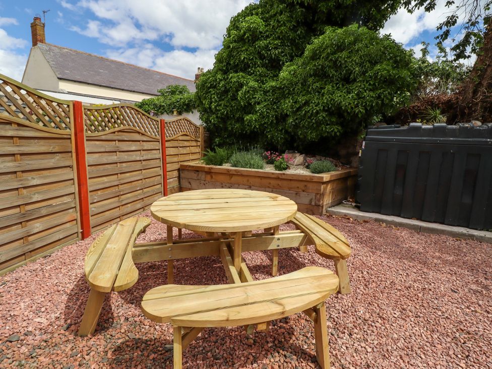 A garden with a wooden table and benches surrounded by gravel and a planter at Sarah's Cottage