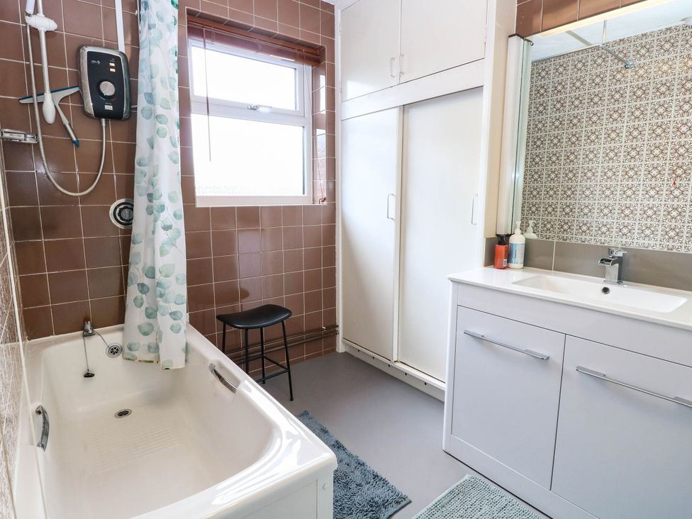 A bathroom with a bathtub, shower, sink, and storage cabinet at The Bungalow in Burgh Castle