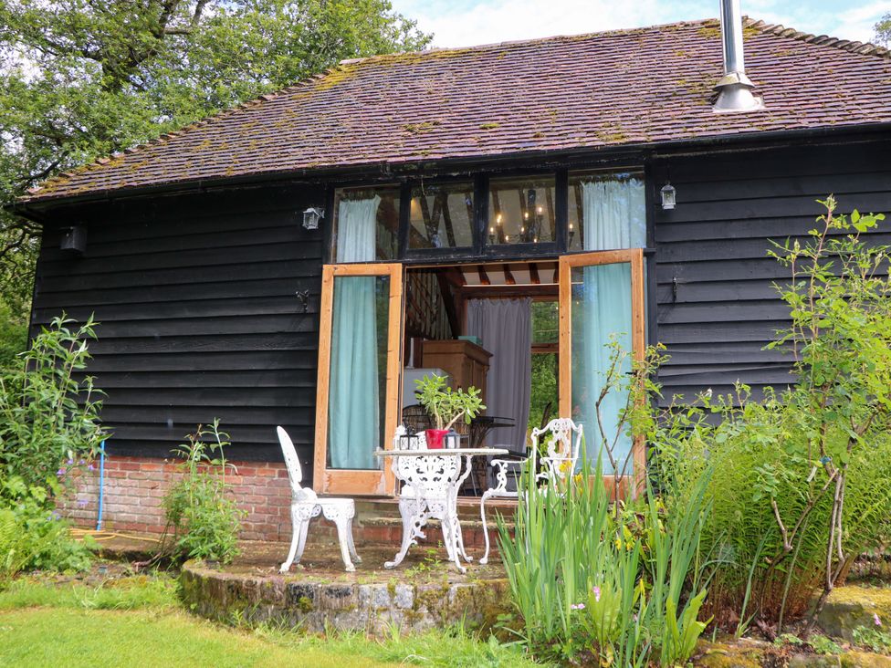 A garden with a wooden building, table, and chairs at Petworth Barn in Petworth