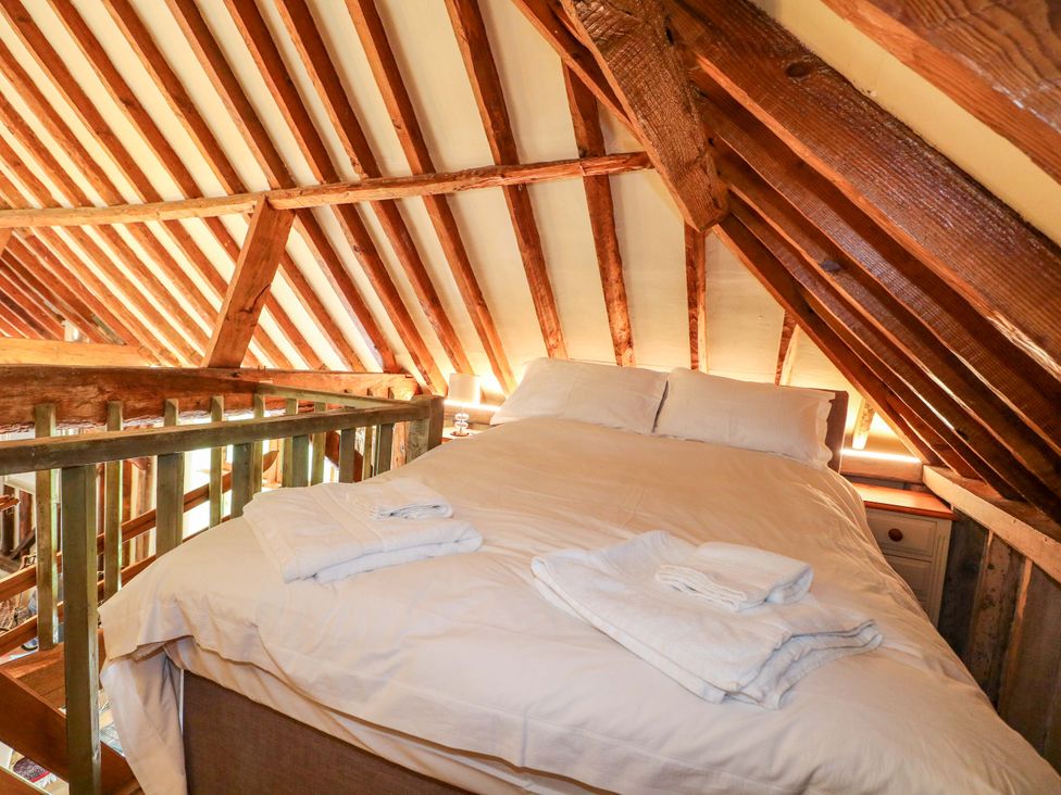 A loft bedroom with a bed and wooden beams at Petworth Barn in Petworth
