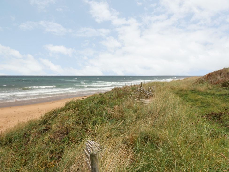 A beach scene with grass and ocean waves at Viola Cottage Fraserburgh