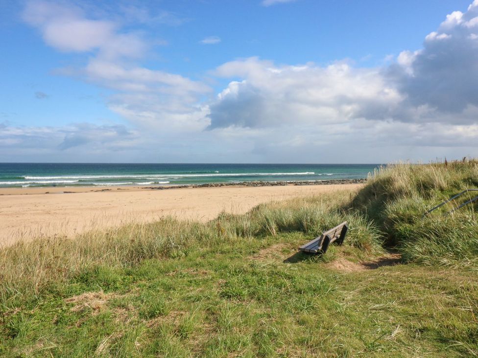A beach with a bench and grass at Viola Cottage in Fraserburgh