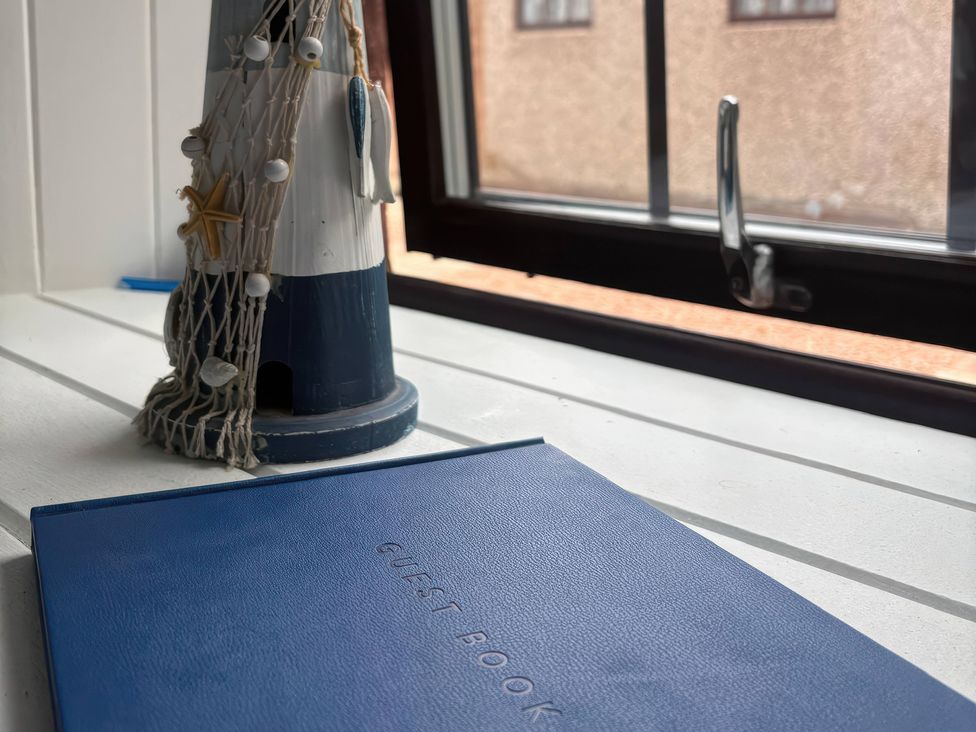 A guest book and decorative lighthouse near a window at Viola Cottage St Combs near Fraserburgh