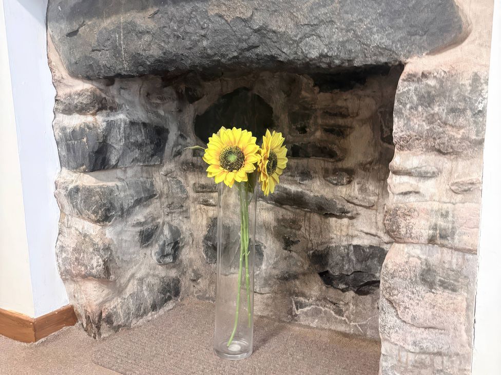 A fireplace with a vase of sunflowers at Viola Cottage St Combs near Fraserburgh