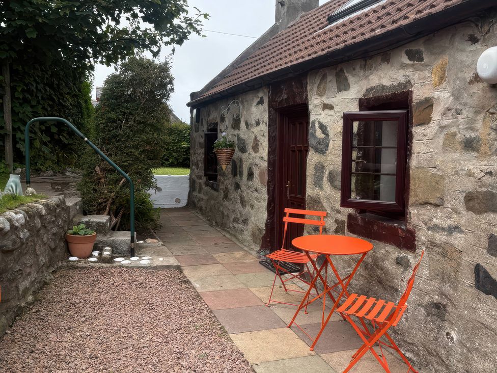 An outdoor area with a stone wall and orange furniture at Viola Cottage St Combs near Fraserburgh
