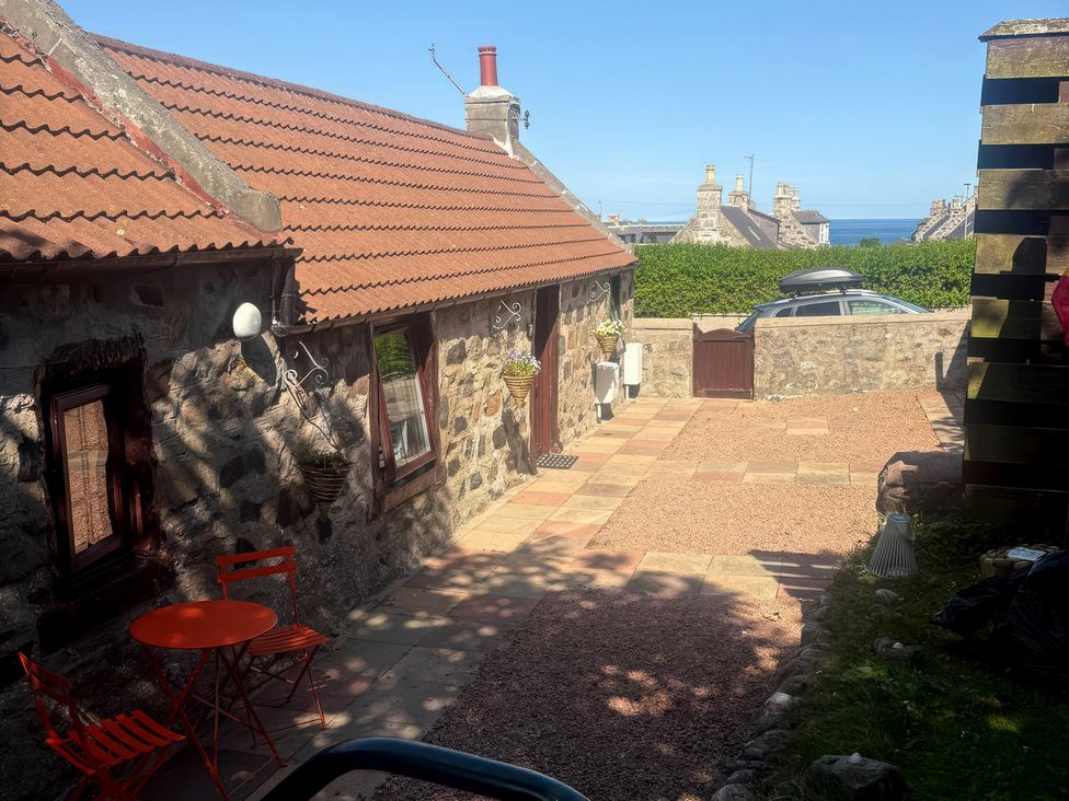 An outdoor area with a stone building and red table at Viola Cottage St Combs near Fraserburgh