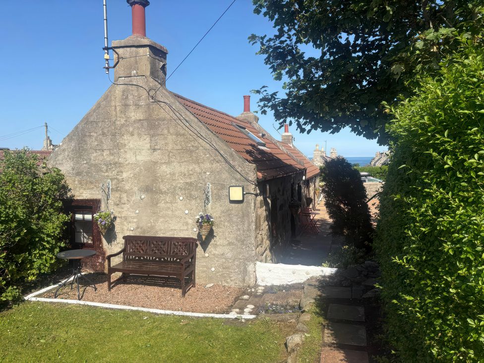 An outdoor view of a house with a bench and table at Viola Cottage St Combs near Fraserburgh